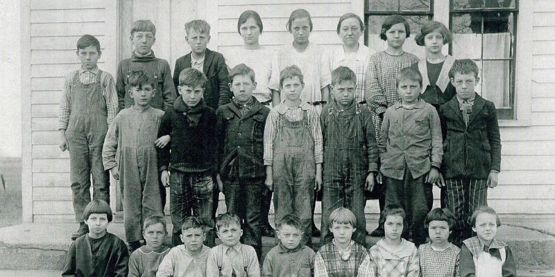 Black and white class photo with two rows of students standing and one row sitting in front of the Moffitt School