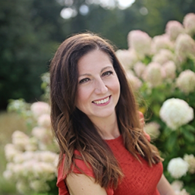 Brunette lady in a red shirt with white flowers and green bushes in the background