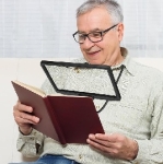 Man using a magnifying reader over a brown book