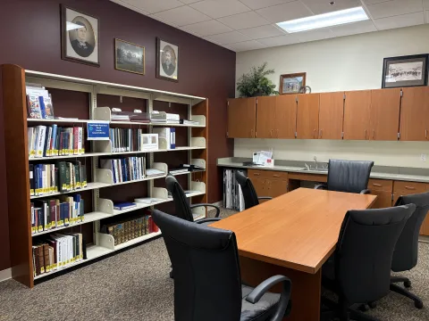 Room with bookshelf along one wall, cabinets along another, and a small board table and chairs in the middle