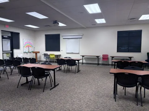 Large room with moveable tables and chairs, whiteboard and projection screen, and podium