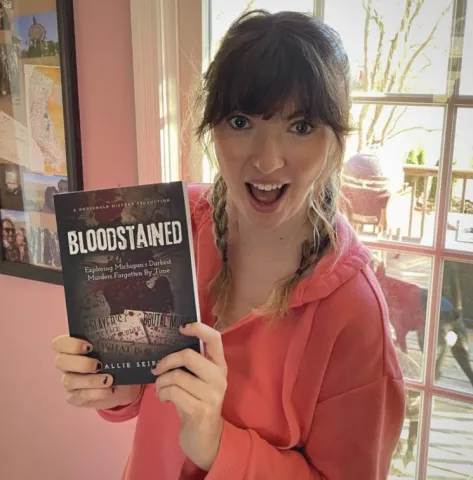Author Allie Seibert holding her book Bloodstained Exploring Michigan's Darkest Murders Forgotten By Time