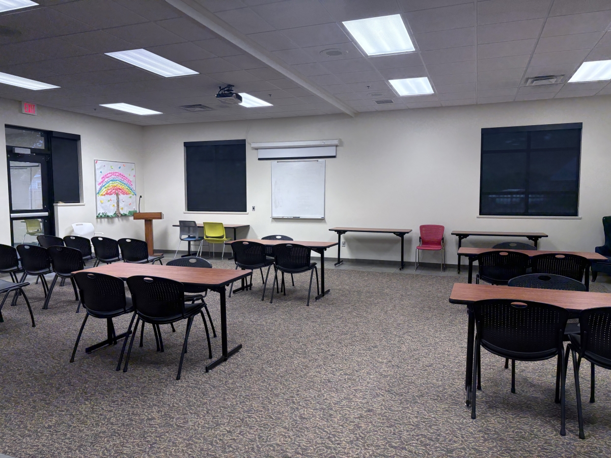 Large room with moveable tables and chairs, whiteboard and projection screen, and podium