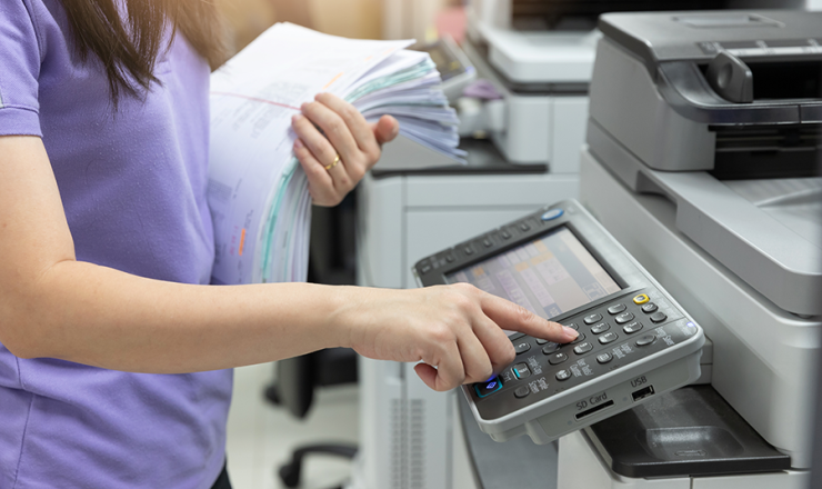 Woman pressing a button on a printer with a stack of papers in her other hands