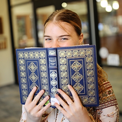 Brunette woman holding a book up over the bottom half of her face