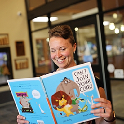 Lady holding a children's book in front of glass windows