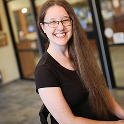 Brunette woman in a black shirt and glasses sitting in front of glass windows