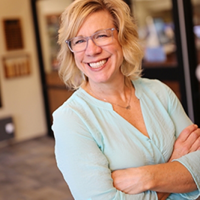 Blonde woman in a blue shirt and glasses with her arms crossed