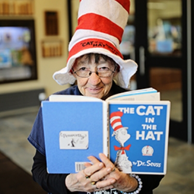 Lady wearing a red and white striped cat in the hat book and holding the Cat in the Hat book